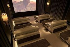 a sophisticated and welcoming home theater with curtains and cool sconces, neutral loungers with pillows and a large screen