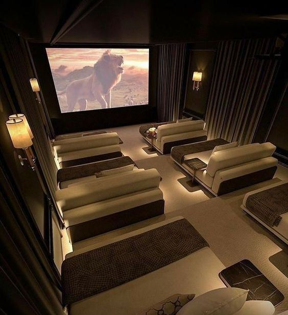 a sophisticated and welcoming home theater with curtains and cool sconces, neutral loungers with pillows and a large screen