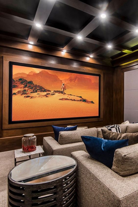 a stylish and chic home theater with stained wooden walls, grey seating furniture, a large screen, built-in lights, shiny side tables
