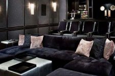 an elegant moody home theater in black, with a large sofa and lots of comfrotable chairs, a pouf and pink pillows, built-in lights