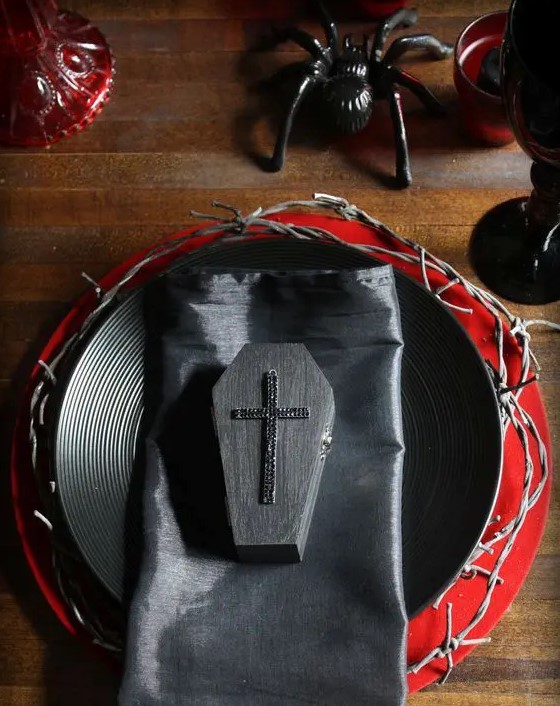 a black and red tablescape with spiders, coffins and textured chargers for a vampire party