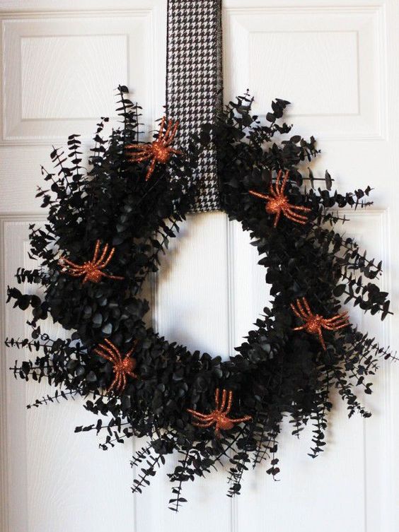 a black foliage wreath decorated with orange glitter spiders, with a printed loop is a lovely decoration for Halloween