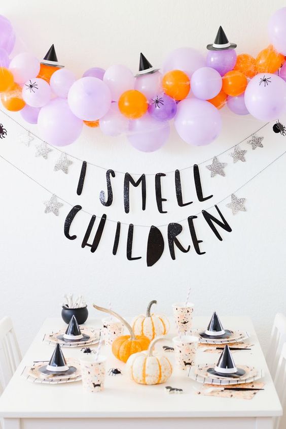 a catchy Halloween party space with lilac balloons, witches' hats, printed cups and plates and a banner