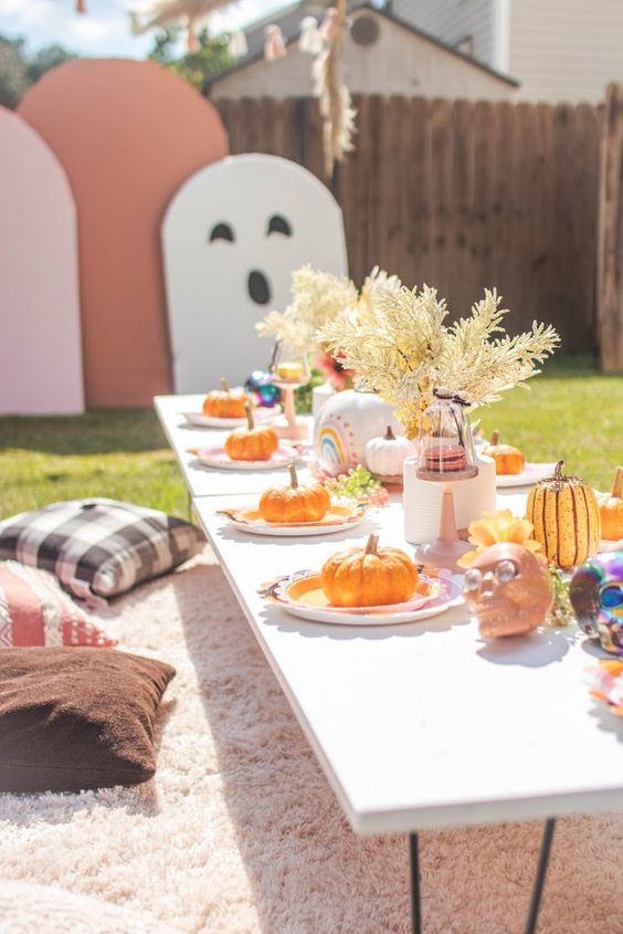 a colorful Halloween kids' party table setting with dried leaves, pastel skulls, pumpkins and a pink rug to sit on