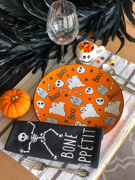a colorful Halloween place setting with a bright orange plate, a black napkin, a bold pumpkin and some feathers