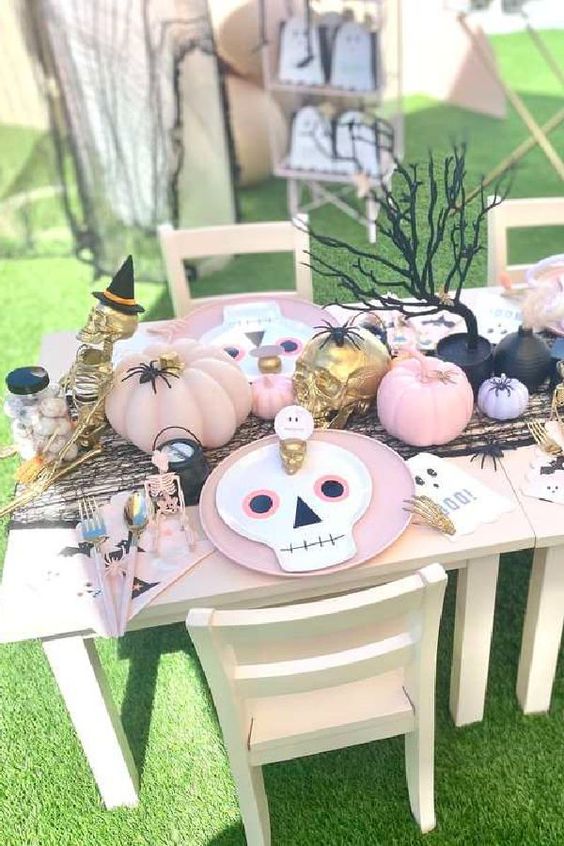 a colorful Halloween tablescape with pink plates and skull ones, pastel pumpkins, gold skulls and a black tree is a lovely idea