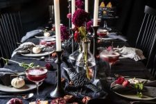 a decadent Halloween tablescape with black linens, crows, bold purple blooms, candles and dried flowers