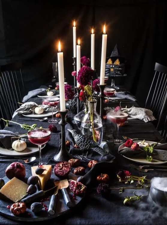 a decadent Halloween tablescape with black linens, crows, bold purple blooms, candles and dried flowers