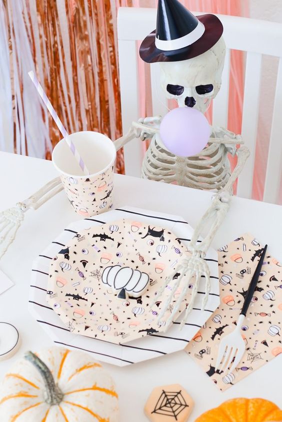 a funny kids' place setting with printed cups, plates and napkins, neutral pumpkins and a small skeleton
