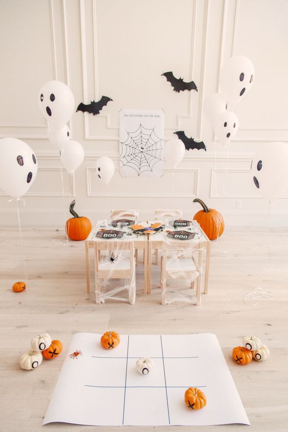 a lovely kids' Halloween party space with ghost balloons, bats, pumpkins and a black and white tablescape done with cheesecloth