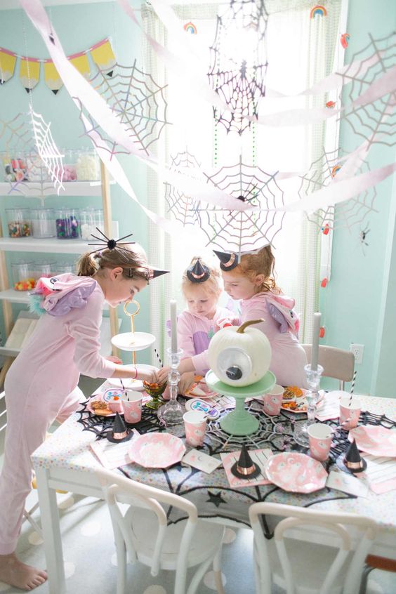 a lovely pastel kids' party table with a googly eye pumpkin, pink ghost plates, black spiderweb placemats and pink paper cups
