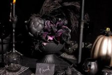 a moody vintage Halloween tablescape with black linens, bright placemats, black candleholders with black candles, a black and purple floral and veggie centerpiece