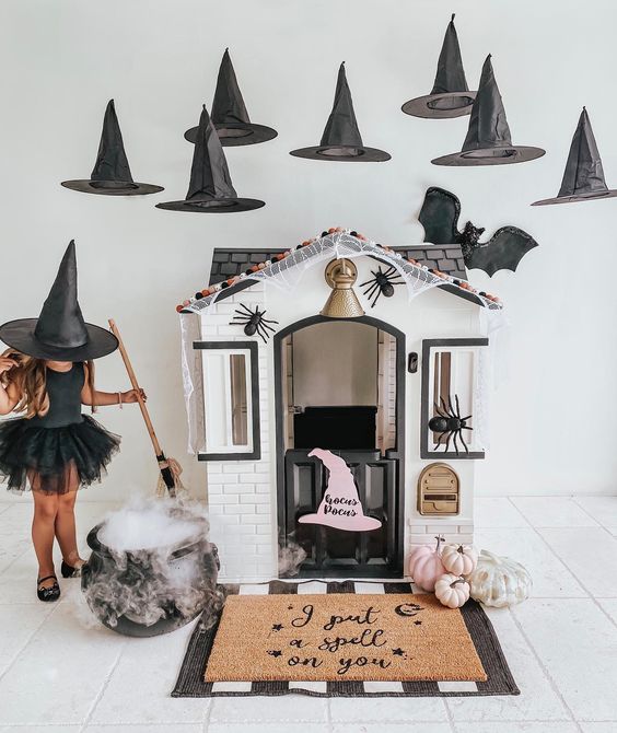 a playhouse with pink pumpkins, witches' hats over it and a cauldron, spiders and layered rugs