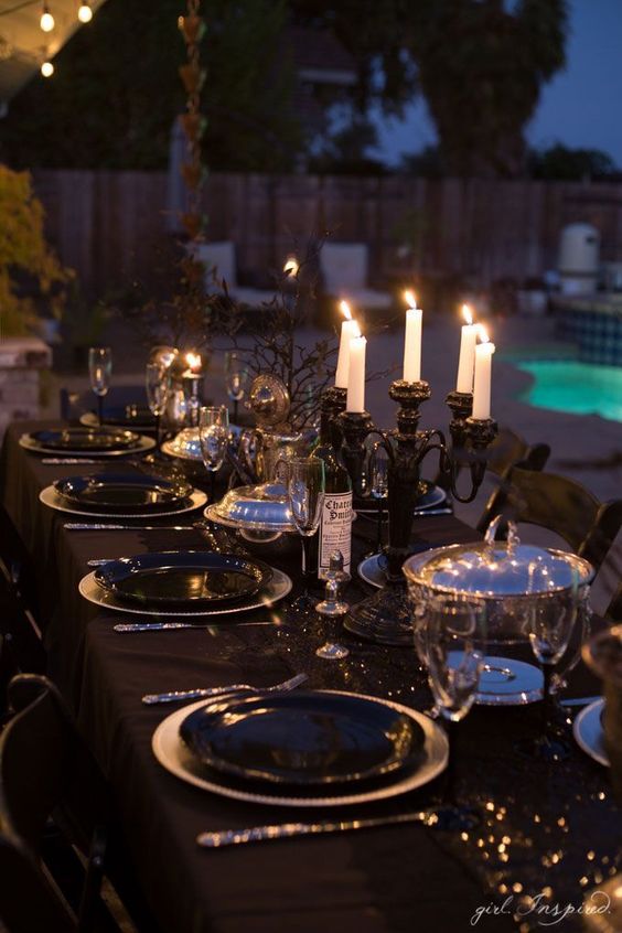 a sophisticated Halloween tablescape with a black tablecloth, plates, candelabras, black branches and shiny metallic touches