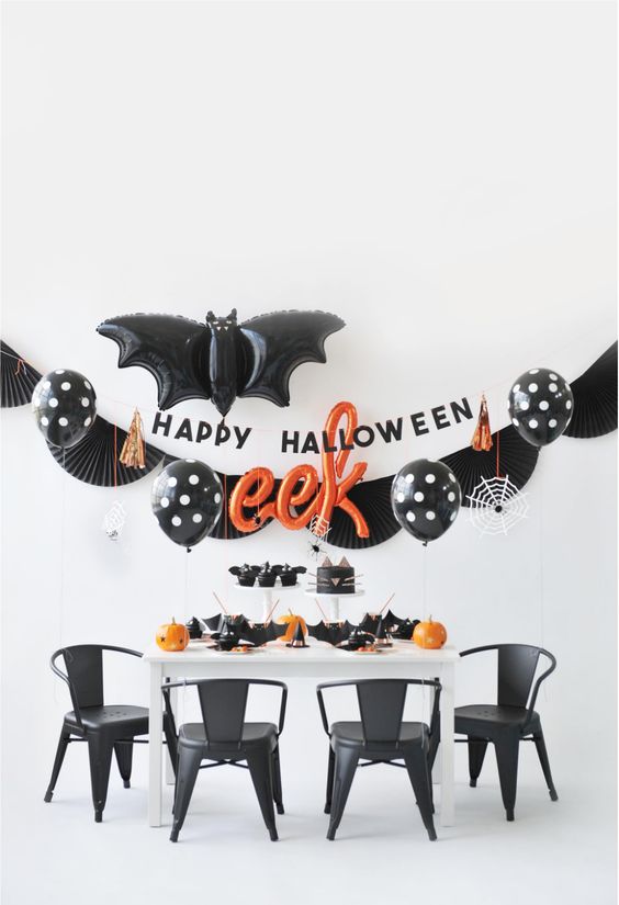 a stylish black, white and orange Halloween space with black balloons, orange pumpkins and black napkins and plates