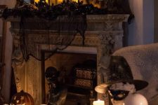 a vintage Halloween fireplace with black spiderweb and pillar candles, vintage candelabras, jack-o-lanterns and black faux blooms