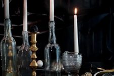 an elegant vintage Halloween tablescape with black and gold plates, tall candles in bottles, chic glasses and dried blooms on the table