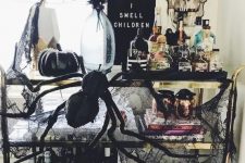 an exquisite Halloween bar cart with a black sign, spiders, black pumpkins, black cheesecloth, dark blooms and lots of drinks