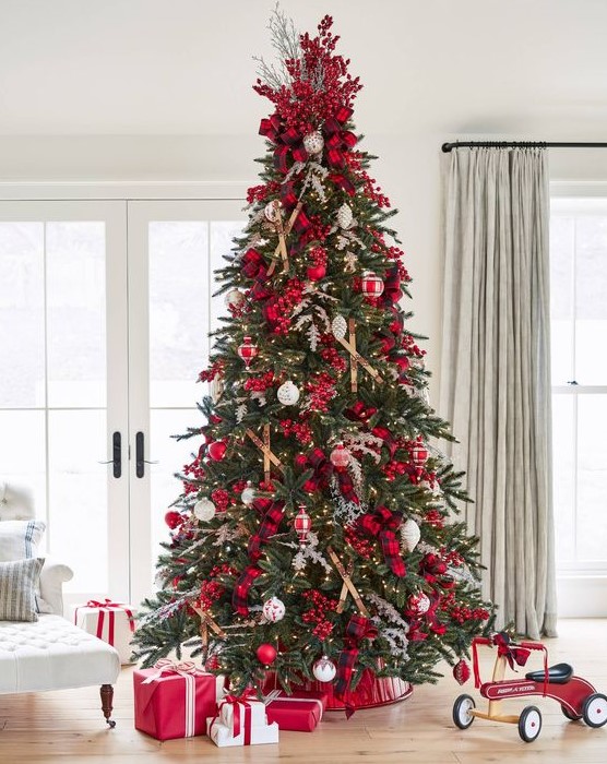 a Christmas tree decorated with lights, red berries, branches, plaid ribbons, red and white ornaments is amazing