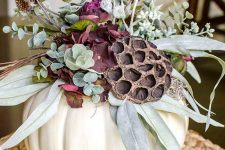 a Thanksgiving centerpiece of a white pumpkin, greenery, lotus, purple blooms and dried blooms is a cool idea