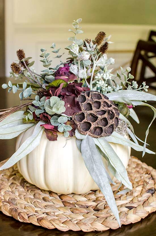 a Thanksgiving centerpiece of a white pumpkin, greenery, lotus, purple blooms and dried blooms is a cool idea