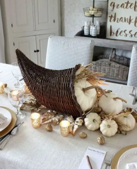 a Thanksgiving centerpiece of a woven cornucopia, white pumpkins, wheat and gilded nuts is a gorgeous idea for your party table