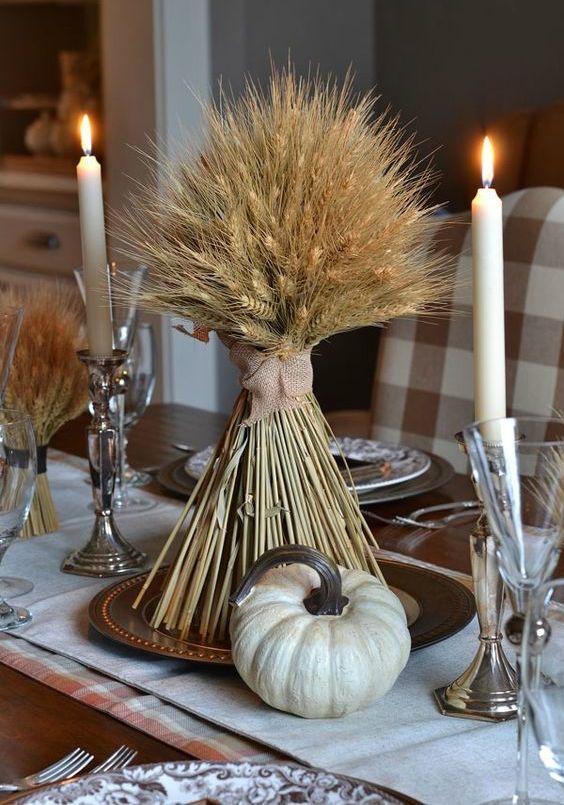 a Thanksgiving centerpiece of wheat, tall and thin candles and a faux pumpkin is a great idea for Thanksgiving decor