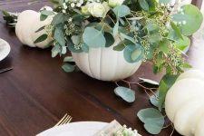 a beautiful and delicate fall centerpiece of a white pumpkin, white blooms and greenery plus some white pumpkins on the table