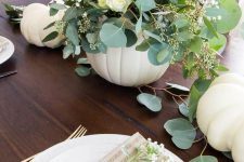 a beautiful and delicate fall centerpiece of a white pumpkin, white blooms and greenery plus some white pumpkins on the table