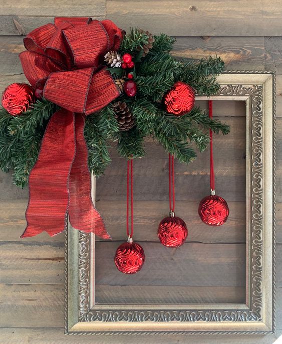 a bold Christmas decoration of a vintage frame, evergreens, red ornaments, pinecones and a large red bow is amazing