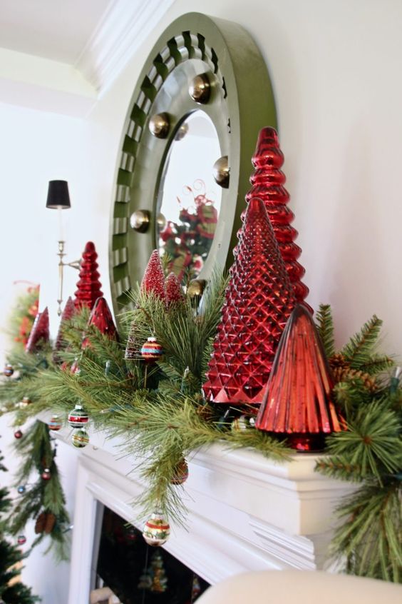 a bold Christmas mantel decorated with evergreens, vintage ornaments, red mercury glass Christmas trees and a mirror in a green frame