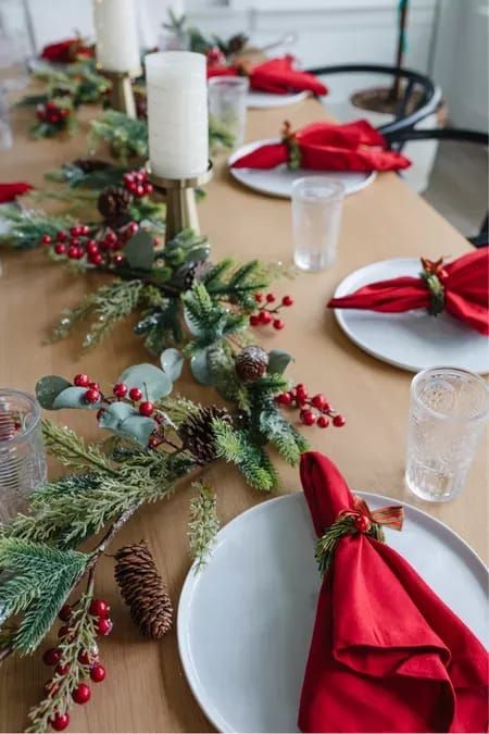 a bold Christmas table setting with an evergreen and pinecone runner, a pillar candle and red napkins plus berries