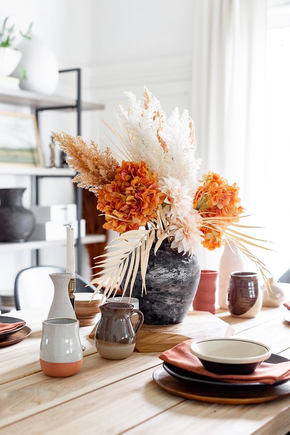 a bold and cool Thanksgiving centerpiece of blush and orange blooms, dried leaves and grasses is awesome