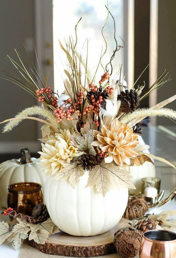 a bold dimensional Thanksgiving centerpiece of a white pumpkin, faux blooms, leaves, berries, real pinecones, twigs and branches