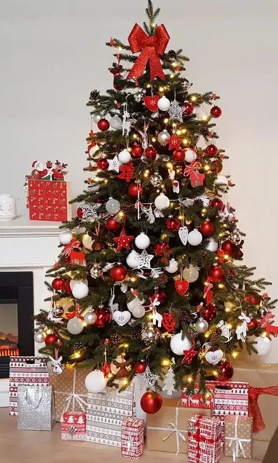 a bold traditional Christmas tree with red and white ornaments of various shapes, lights and with a red bow on top