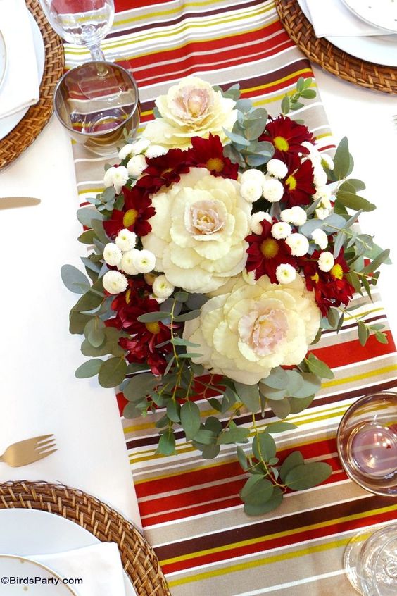 a bright Thanksgiving centerpiece of neutral and burgundy blooms, greenery and candles around is amazing