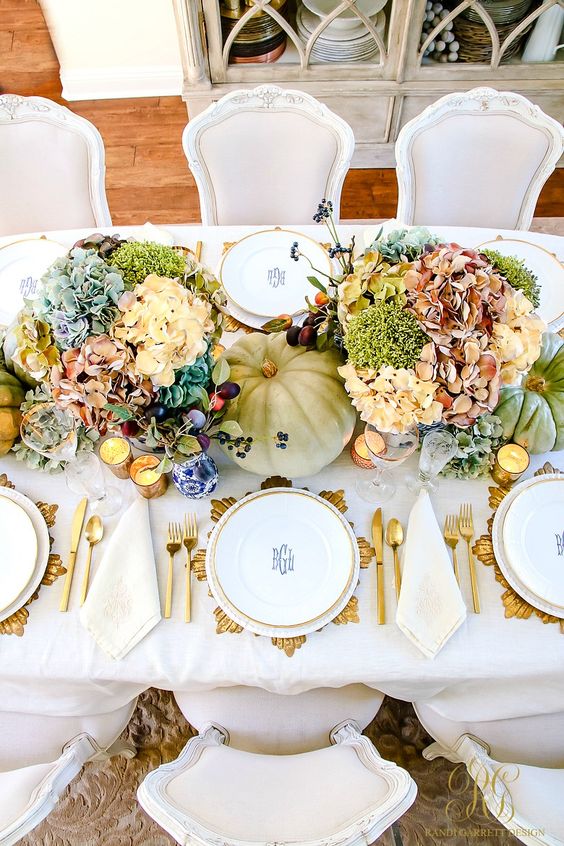 a bright Thanksgiving centerpiece of pink, neutral, blue flowers, greenery, green pumpkins and berries is a lush and cool idea