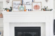 a bright Thanksgiving mantel with bold signs, greenery and mini pumpkins and matching pillows at the fireplace