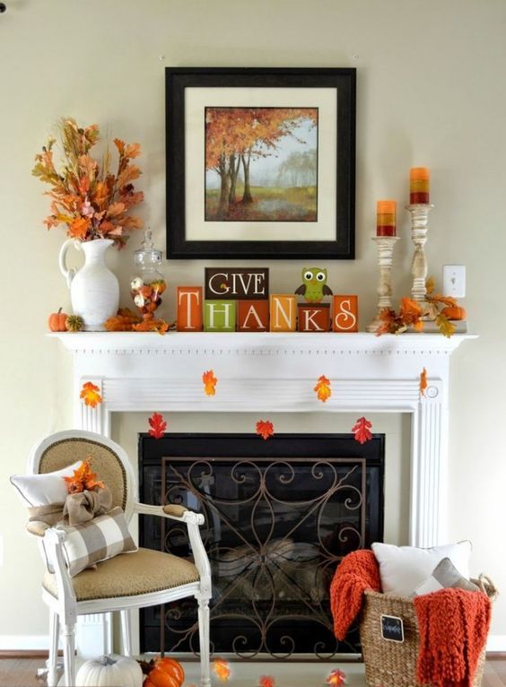 a bright Thanksgiving mantel with colorful leaves, colorful striped candles, bright cubes, dried leaf arrangements and blankets and pillows