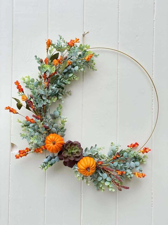 a bright fall or Thanksgiving wreath partly decorated with faux greenery, bold orange blooms, mini gourds and a succulent is chic