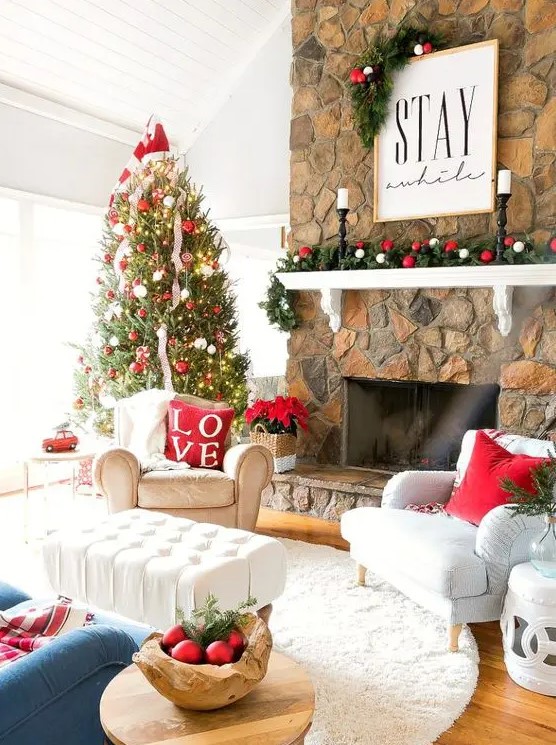 a bright holiday living room with a Christmas tree decorated with red and white ornaments, with a matching garland, red pillows and ornaments