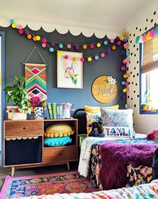 a bright kid's room with a black wall, colorful pompom garlands, pillows, bedding and a rug is extra bold