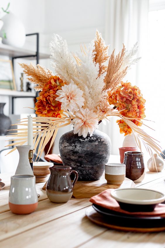 a bright modern Thanksgiving centerpiece of orange and blush blooms and dried grasses is a gorgeous idea for your party