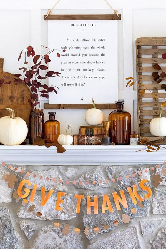 a chic and bold Thanksgiving mantel with white pumpkins, dark leaves, apothecary bottles, a quote and some wooden decor