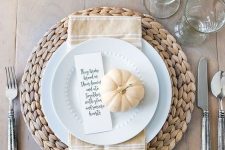 a chic neutral Thanksgiving place setting with a wovne placemat, white porcealin, a tan npkin and pumpkin plus a card