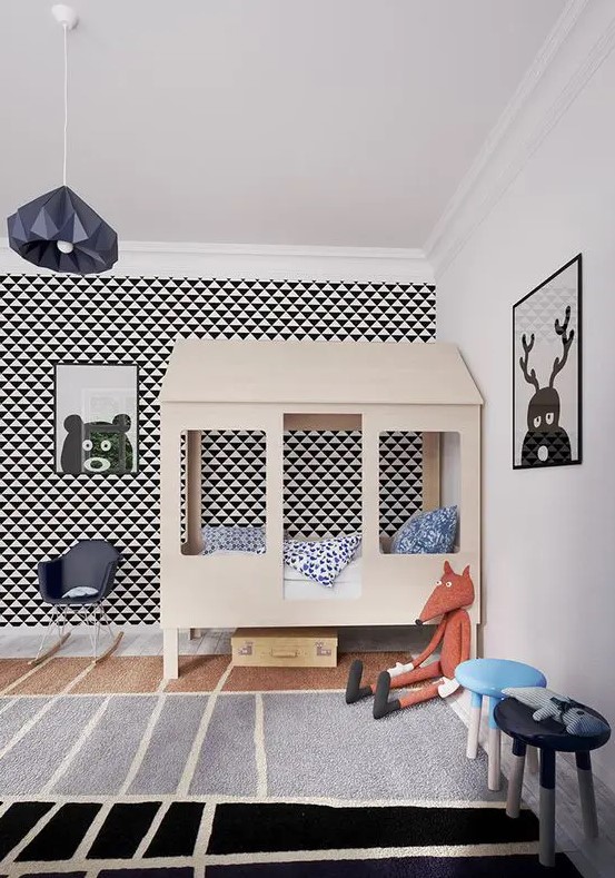 a cool and whimsical kid's room with a geo accent wall, a plywood house bed, cool artworks, a faceted pendant lamp and some lovely toys
