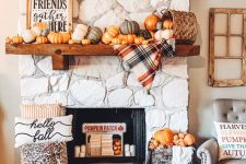 a cozy and chic Thanksgiving mantel with lots of pumpkins, a basket, a plaid blanket, a sign and some pumpkins in a crate