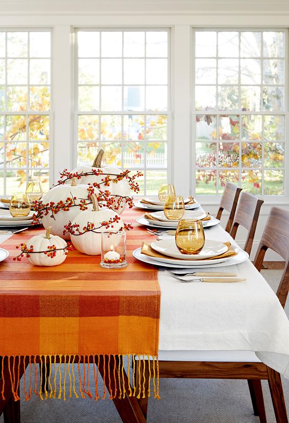 a cozy and simple Thanksgiving centerpiece of white pumpkins and bold berries accented with a bold matching table runner is a cool idea