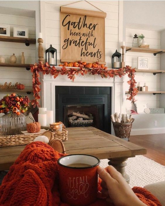 a cozy rustic Thanksgiving mantel with a bold leaf garland, orange pumpkins, a paper hanging and candle lanterns