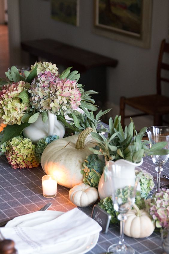 a delicate Thanksgiving centerpiece of green and pink hydrangeas, white pumpkins and some greenery in jugs